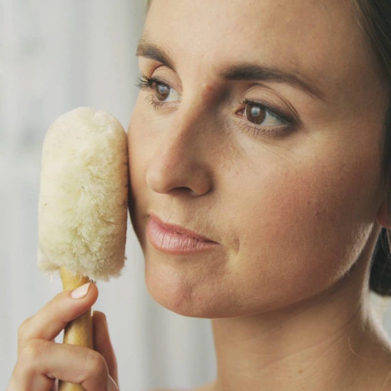 Woman holding a brush near her face against a neutral background