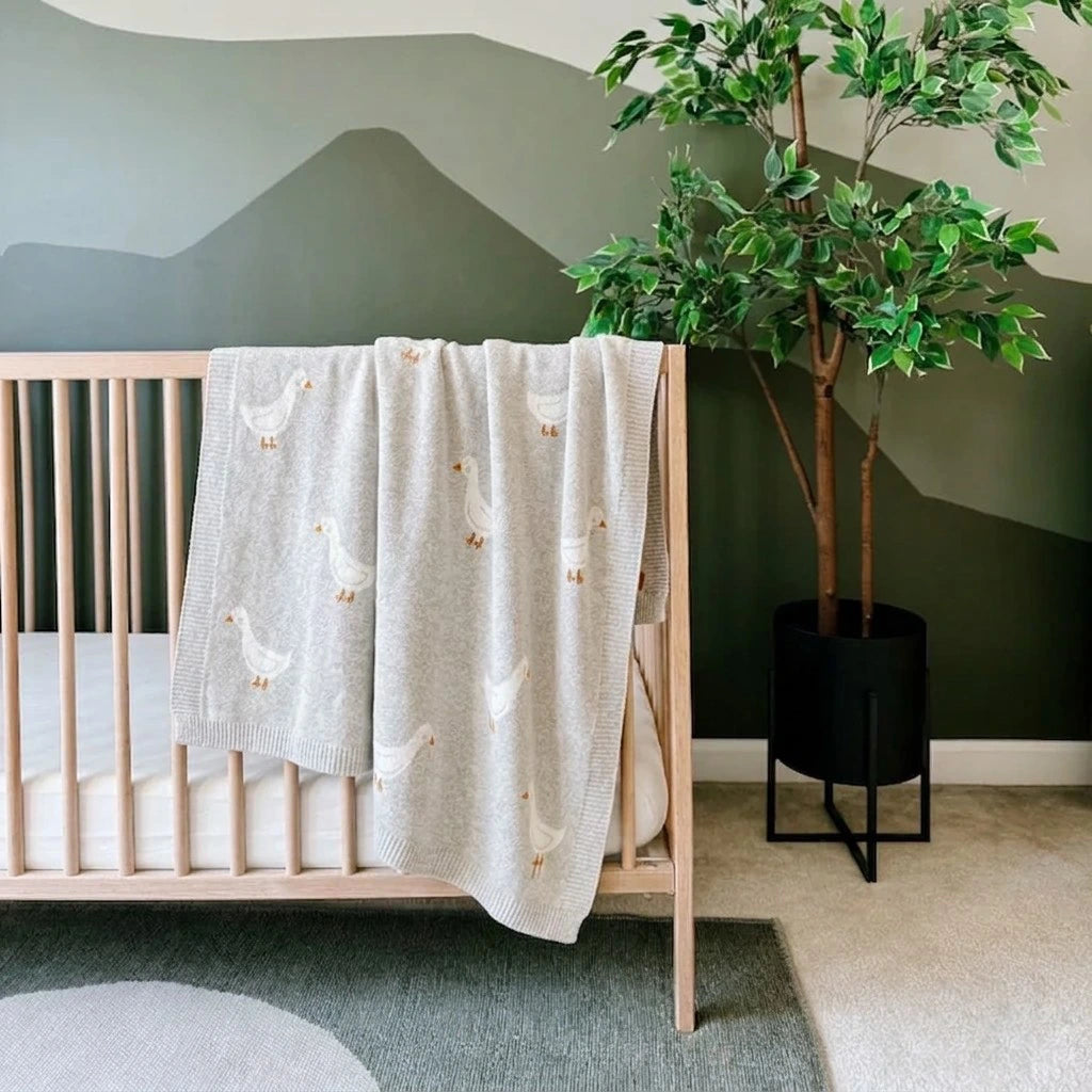 Nursery room with a crib, decorative goose blanket, and potted plant.