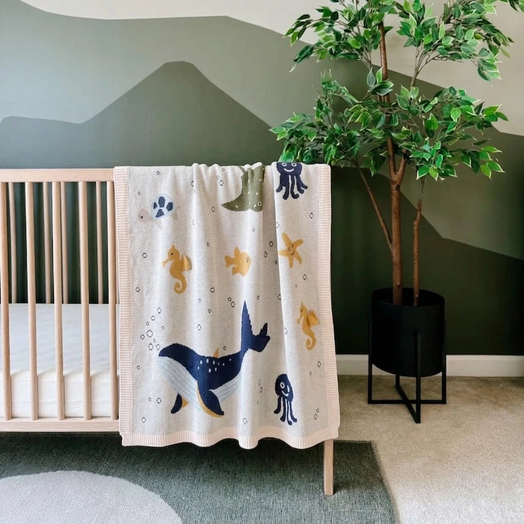 Nursery room with a crib and decorative blanket featuring marine animals.