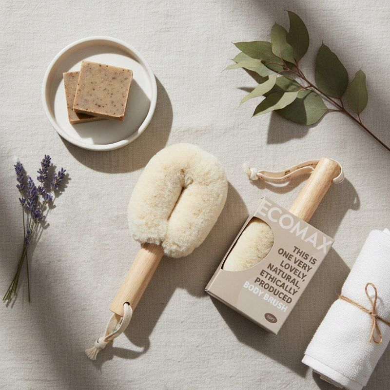 Ecomax body brush with packaging, soap, and towel on a neutral background