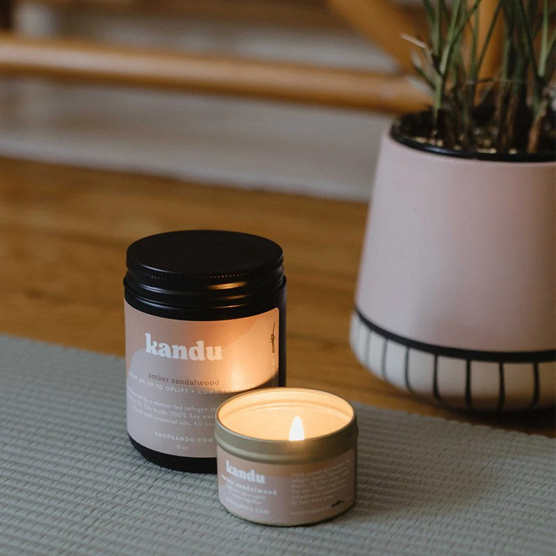 amber sandalwood candle lit on a table with plant in the background