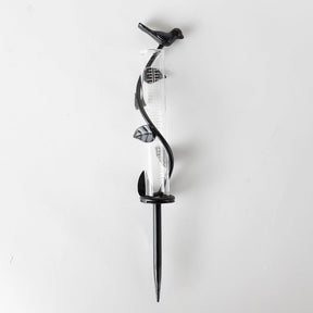 Glass rain gauge with black metal stand on a white background
