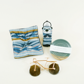 Collection of kitchen tools including a sea otter skillet handle, a ceramic greater grater, a stainless steel bicycle pizza cutter, and a woven cotton microwave cozy.