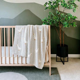 Nursery room with a crib, decorative goose blanket, and potted plant.