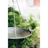 Decorative bird bath with a small bird ornament hanging over it, set against a blurred green outdoor background.