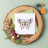 Quilled greeting card with a colorful butterfly design on a wooden surface with flowers and leaves.