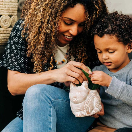 Woman and child sitting together, looking at a small ceramic cat pot.