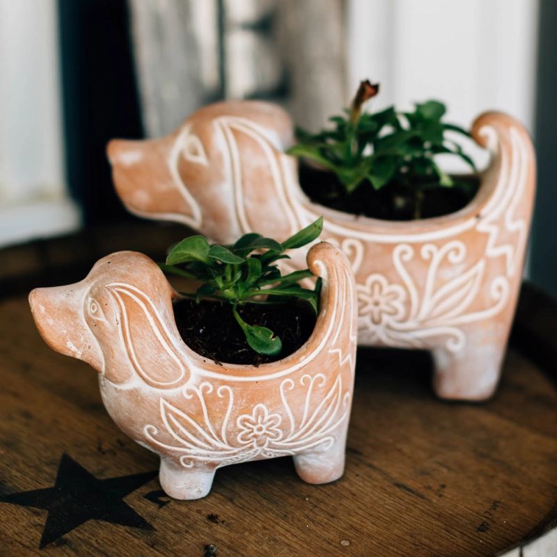 Two dog-shaped ceramic planters with plants inside on a wooden surface.