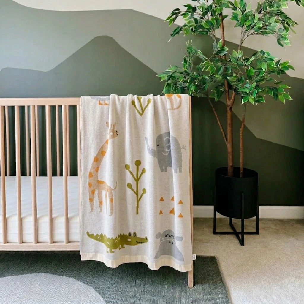 Nursery room with crib and animal-patterned blanket, green wall, and potted plant.