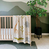 Nursery room with crib and animal-patterned blanket, green wall, and potted plant.