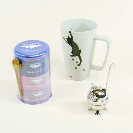Tea canister, mug with cat design, and tea ball infuser on a white background