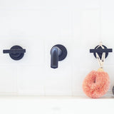 Black bathtub faucet on a white wall with a pink spa bursh hanging from one of them.