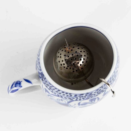 Blue and white ceramic mug with cat-shaped metal tea infuser on a white background