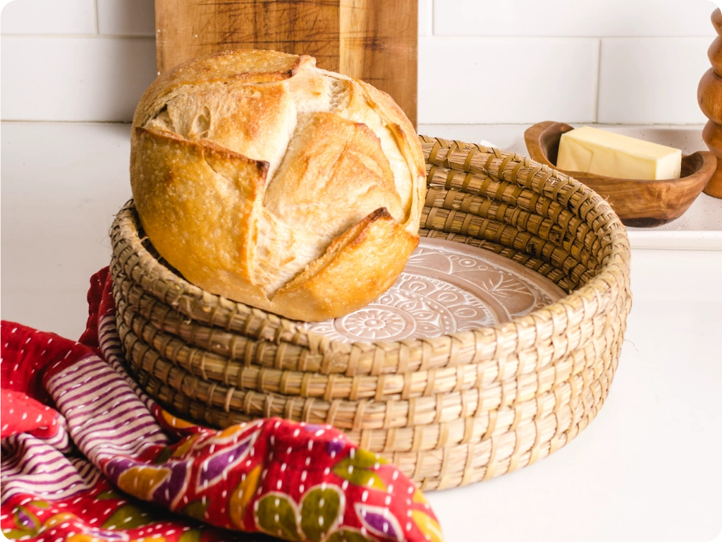 Loaf of bread in a woven basket on a kitchen counter with a colorful towel.