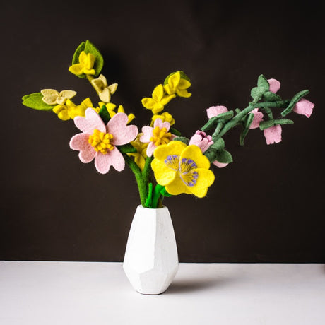 Sustainable felt flower stems in mixed colors including pink, yellow, and green in white vase on against a dark background