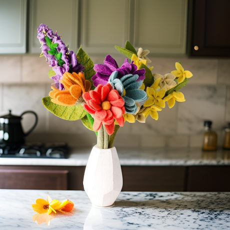 Colorful felt flower bouquet in a white vase on a kitchen counter.