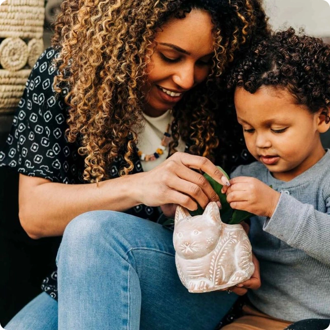Mother and child sitting together, looking at a small ceramic cat pot - mother's day gardening gifts